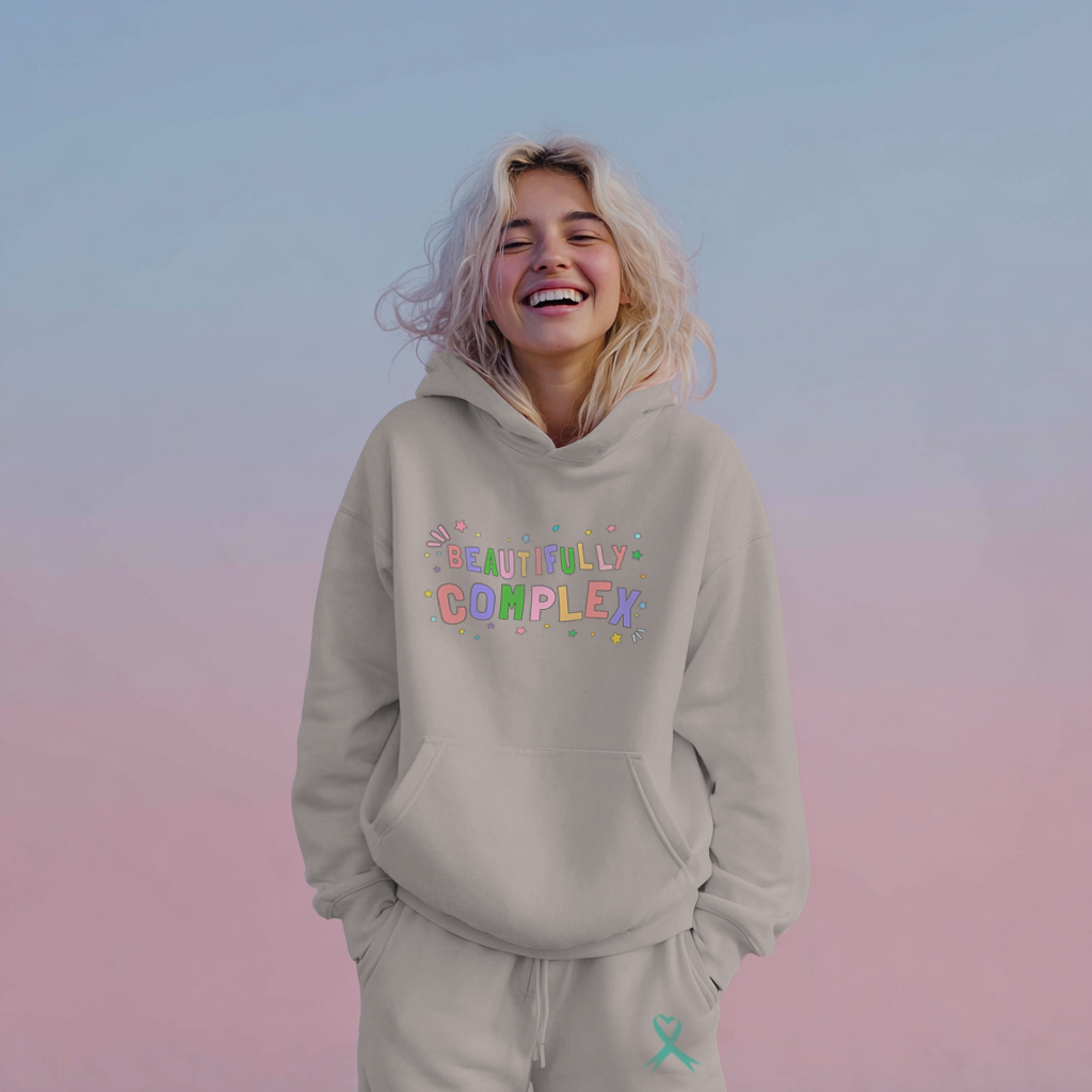 Person wearing a beige hoodie with 'BEAUTIFULLY COMPLEX' text on a gradient background